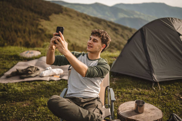 istock Young boy sit in front tent and video call or selfie on the mountain 2159052241