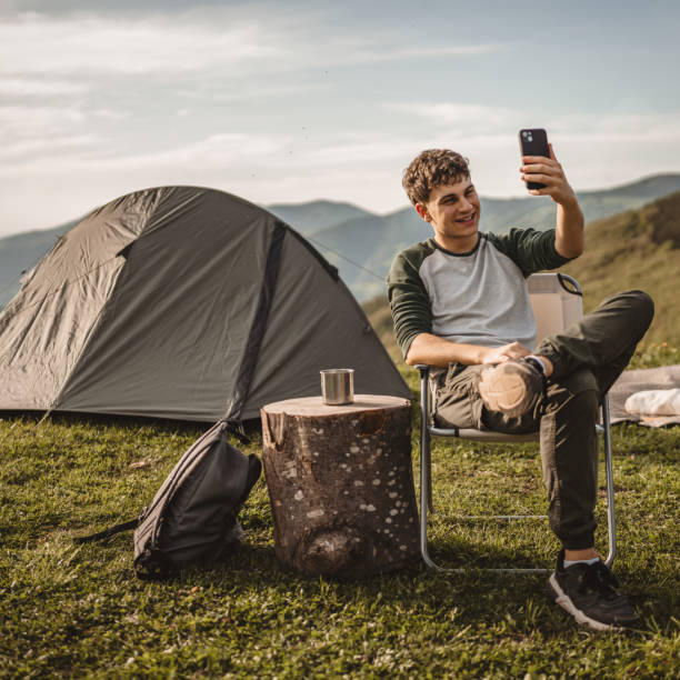 istock Young boy sit in front tent and video call or selfie on the mountain 2159053014