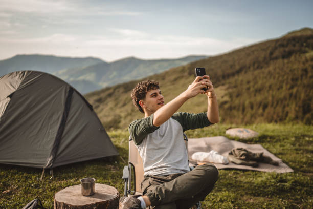 istock Young boy sit in front tent and video call or selfie on the mountain 2159053123