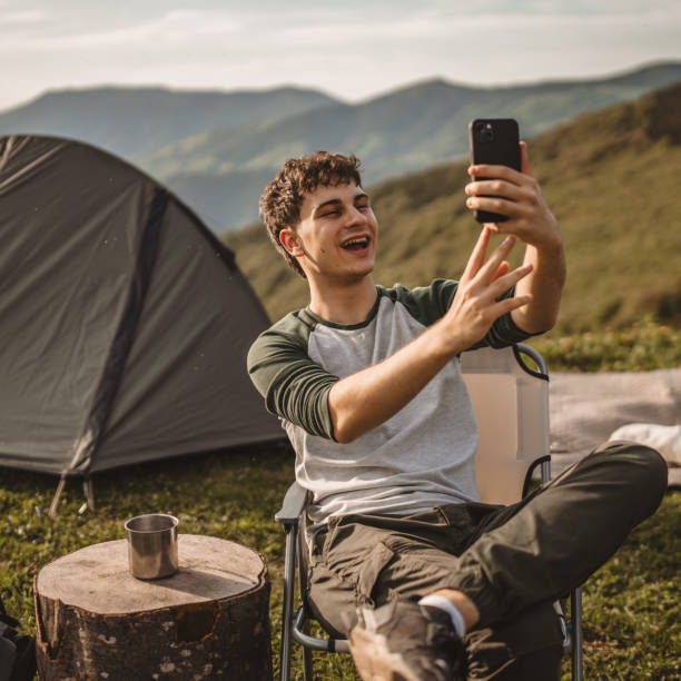 istock Young boy sit in front tent and video call or selfie on the mountain 2159053536