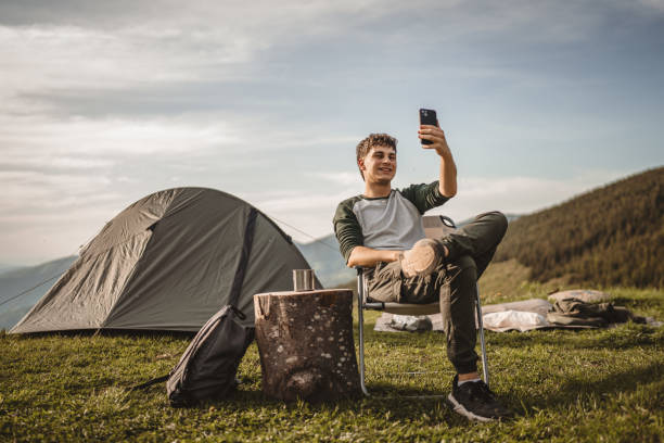 istock Young boy sit in front tent and video call or selfie on the mountain 2159053961