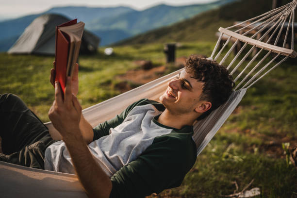 istock Young boy lying down in a hammock on the mountain and read a book 2159054107