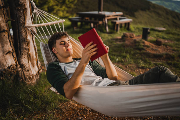 istock Young boy lying down in a hammock on the mountain and read a book 2159054245