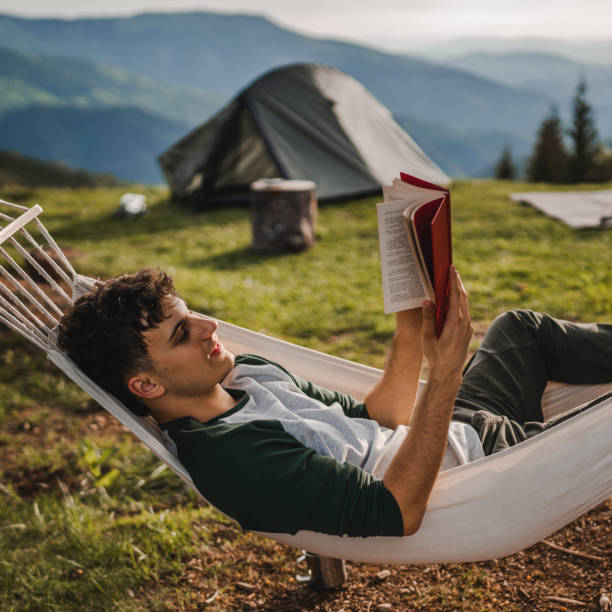 istock Young boy lying down in a hammock on the mountain and read a book 2159055124