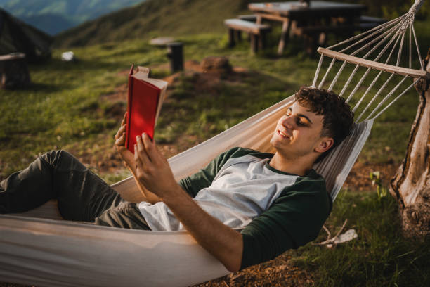 istock Young boy lying down in a hammock on the mountain and read a book 2159055135