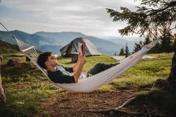 istock Young boy lying down in a hammock on the mountain and read a book 2159055200