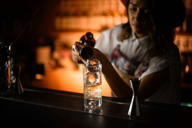 istock Female bartender pours a drink from a jigger into a tall glass 2159064908