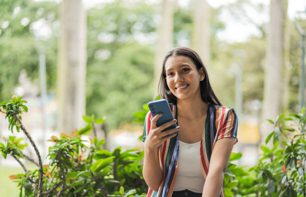 istock latina woman outdoors using her cell phone and smiling 2159066640