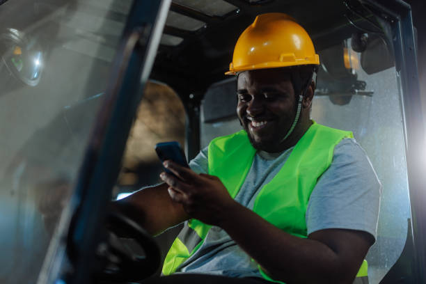 istock Worker sitting in a forklift, looking at his phone and smiling. 2159067766