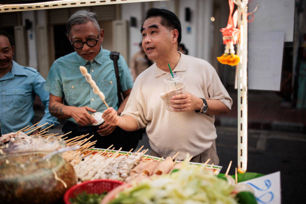 Male friends buying Thai food in a street food marketplace in Bangkok, Thailand.