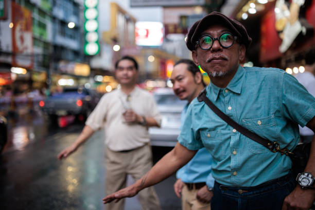 Male friends standing on the street and trying to catch a ride on a rainy day in Bangkok, Thailand.