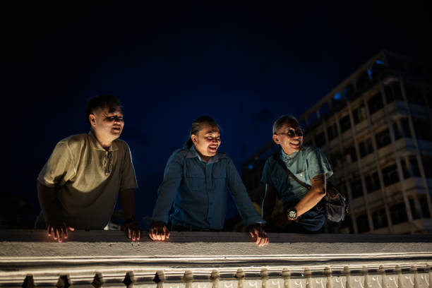Three men standing by the edge of a rooftop during twilight in Bangkok, Thailand.