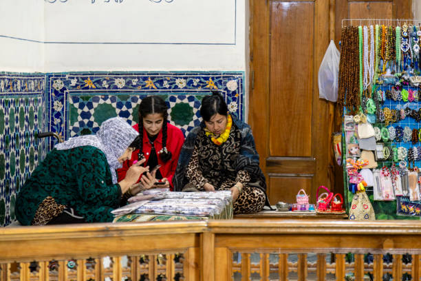 Samarkand, Uzbekistan. May 17th, 2024. Uzbekistani women selling souvenirs, one of them using smartphone, inside the Bibi Khanym Mausoleum in Samarkand, UNESCO world heritage site.