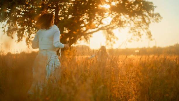 istock Serene Sunset Stroll with Mother and Daughter by Meadow Tree 2159082133