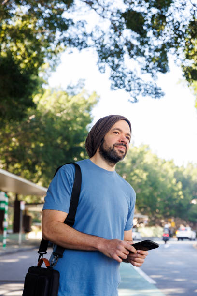 istock Man Using Phone At Suburban Bus Stop - Looking Out At Environment 2159083331