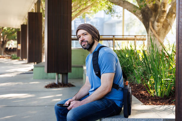 Man Using Phone At Suburban Bus Stop - Looking Out At Environment