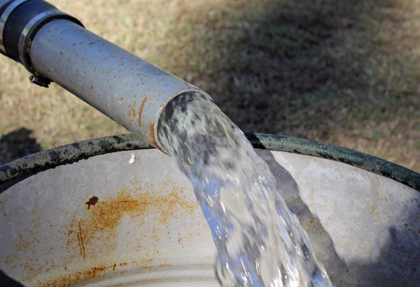istock Close up view of water flowing from a metal pipe into a large container 2159088570