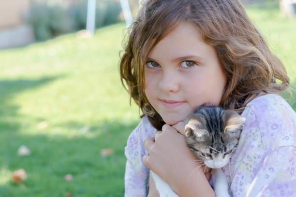 pretty long-haired blonde girl cuddling her cat with a sunlit green meadow in the background and copy space