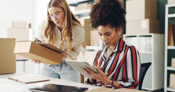 istock Women, tablet and teamwork with boxes, package and e commerce checklist for online shop, stock or supply chain. Young people with small business and digital tech or clipboard for logistics and order 2159117387