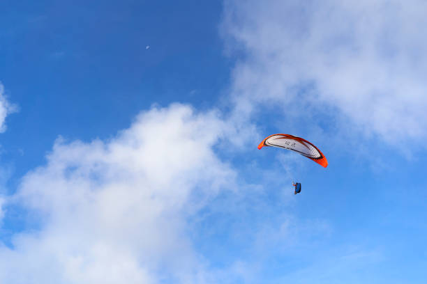 France, Normandy - October 06, 2024: A paraglider soars in the sky, suspended under an orange, white, and black wing, capturing the sense of freedom and adventure in paragliding.
