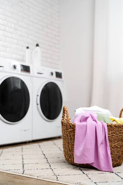 istock Laundry Basket With Clean Clothes in Front of Modern Washing Machines 2159122598