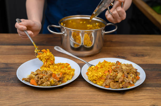 istock Lunch time, wife puts potted dinner on plates, rice with chicken in curry sauce 2159124190