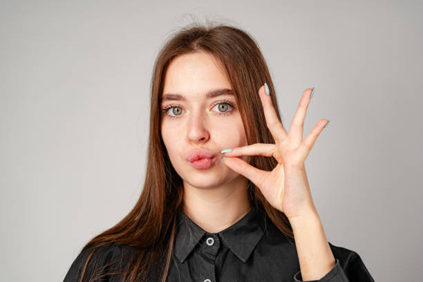 istock Smiling Young Woman Posing With Finger on Lips Against Grey Backdrop 2159125699