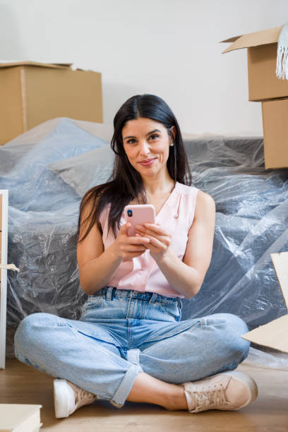 istock Woman is sitting on the floor using smartphone surrounded by cardboard boxes 2159125748