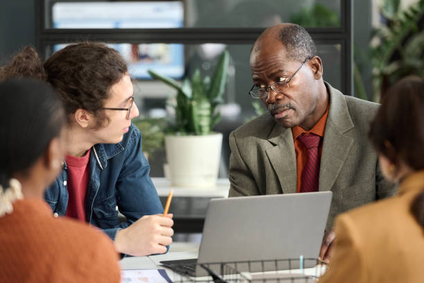 istock Black Senior Businessman Looking at Young Coworker 2159129487