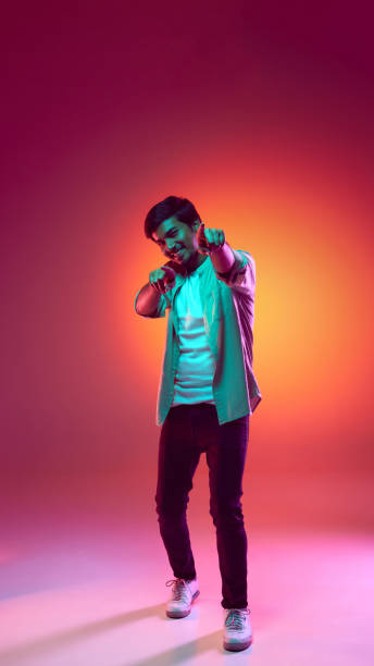 istock Young man exudes confidence and playfulness as he points directly at camera in neon light against gradient studio background. 2159129693