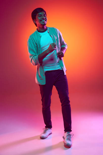 istock Young man radiates joy and enthusiasm as he strikes a dance pose in neon light against gradient studio background. 2159129696