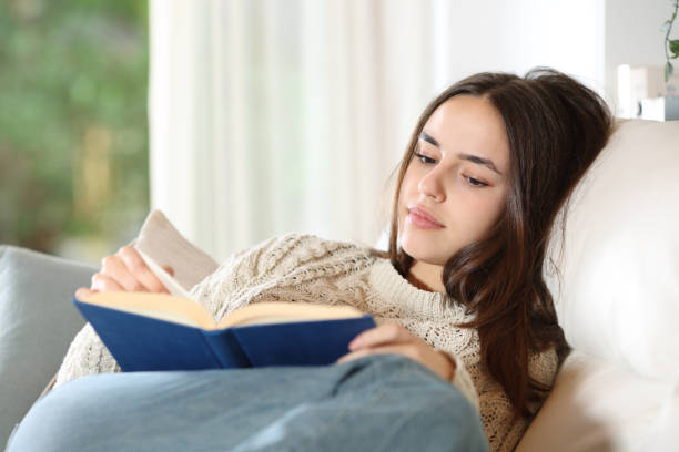 istock Serious woman reading paper book on a couch 2159131927
