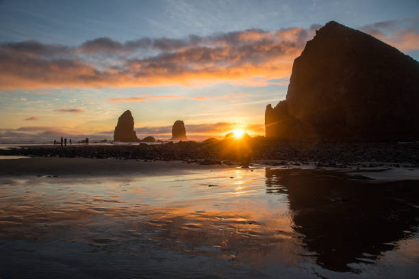 Cannon Beach, Oregon, sunset, water reflections, adventure, outdoors, beautiful, landscape, scenic, Pacific Ocean, coastline, Haystack Rock, golden hour, serene, tranquil, breathtaking, panoramic, waves, shoreline, sandy beach, tide pools, dramatic sky, colorful, horizon, twilight, nature, picturesque, natural beauty, exploration, sea stacks, rugged, coastal, scenery, west coast, vacation, travel, beachcombing, hiking, romantic, seascape, dusk, peaceful, photography, stunning, clouds, evening light, sun rays, surf, relaxation, getaway, marine life