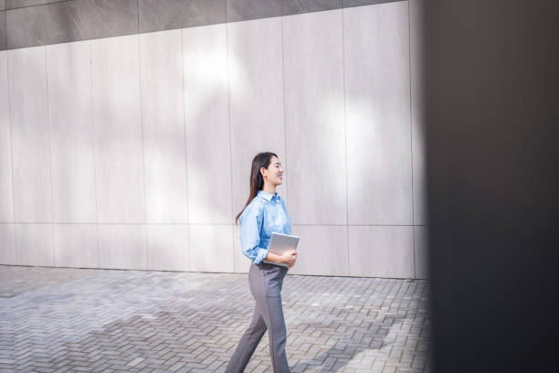 istock Asian woman using laptop while walking outside in a modern urban area. 2159135952