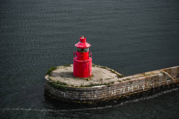A red lighthouse stands on a stone breakwater in the waters off of Copenhagen, Denmark.