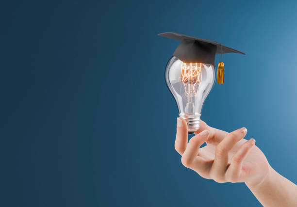 istock Hand Holding Light Bulb with Graduation Cap on Blue Background 2159142579