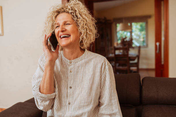 istock Happy middle aged woman doing a phone call relaxing on sofa at home 2159143496