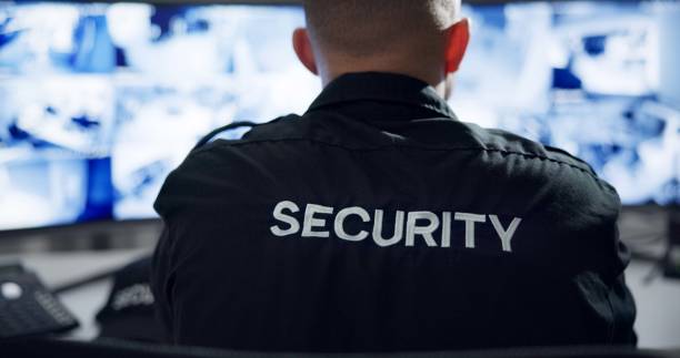 istock Security guard, computer screen and watch by cctv monitor for protection, data center or building safety. Inspection, video surveillance agency and control room with footage, technology and rear view 2159146678