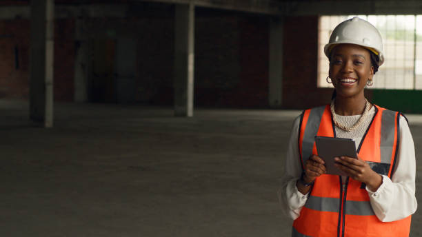 Confident Female Engineer in Hard Hat and Safety Vest Inspecting Construction Site with Digital Tablet