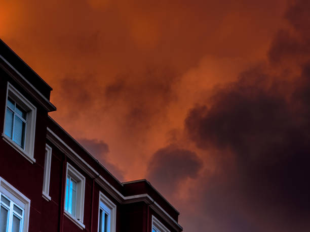 The silhouette of an apartment building against a stunning sunset sky filled with dark clouds glowing orange and red.