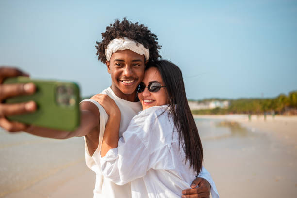 istock Joyful Hispanic Woman and Black Man Taking Beach Selfie 2159151469