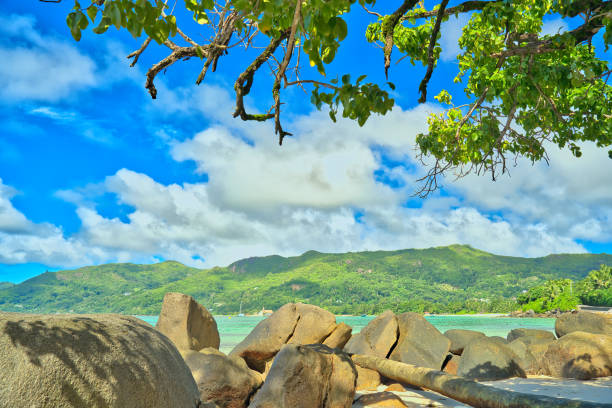 Anse Royale beach, Mahe, blue sky turquoise water, low tide sunny day, white sandy beach and granite rock boulders, Seychelles mountain in the background