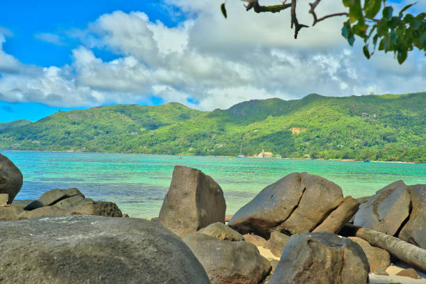 Anse Royale beach, Mahe, blue sky turquoise water, low tide sunny day, white sandy beach and granite rock boulders, Seychelles mountain in the background