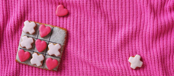 istock Vibrant pink wallpaper with a gingerbread tic-tac-toe game on a cozy knitted sweater backdrop. Valentine's Day Conception. Romantic Background 2159152271