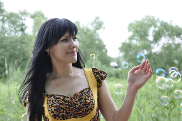 A brunette girl catches soap bubbles in the summer. She laughs, it's hilarious. Catching them with her hands, there is joy on her face