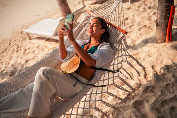 istock Relaxed Hispanic Woman Taking Selfie on Beach Hammock 2159165163