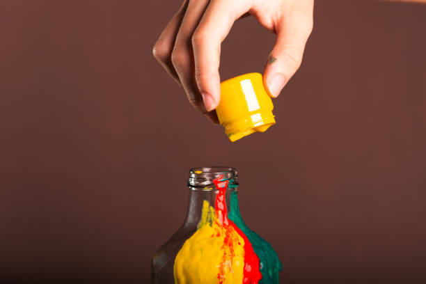 Painter pouring yellow paint into a glass bottle. abstract art. Isolated on brown background.