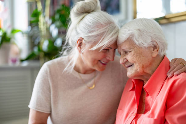 happy senior woman with her adult daughter at home - ouderenzorg stockfoto's en -beelden