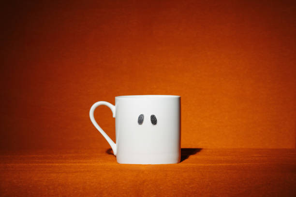 White mug with sparkly spooky ghost eyes on orange background. Creative minimalist Halloween wallpaper