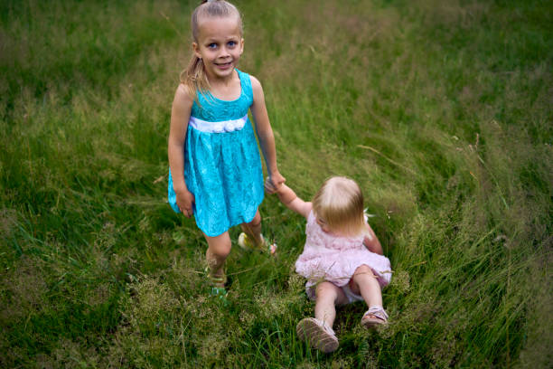 two little sisters in dresses playing together in the tall grass